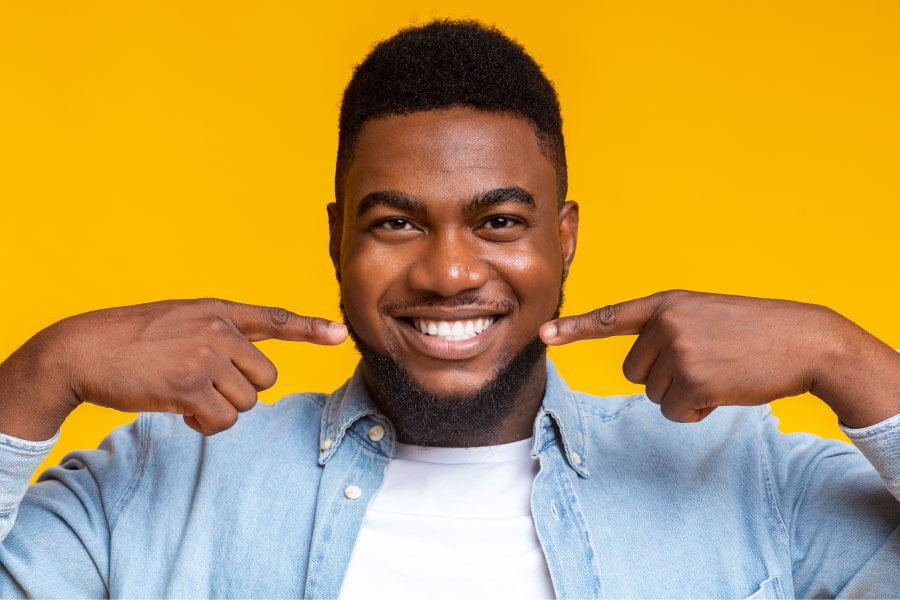 Dark-haired man smiles after cosmetic dentistry and points to his teeth in Broken Arrow, OK