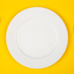 Aerial view of a white plate and silverware on a yellow table