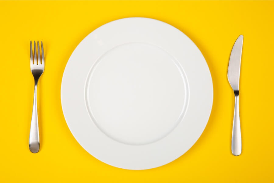 Aerial view of a white plate and silverware on a yellow table