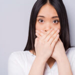 Dark-haired woman covers her mouth with her hands due to chronic bad breath