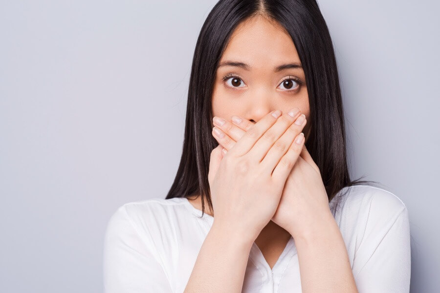 Dark-haired woman covers her mouth with her hands due to chronic bad breath