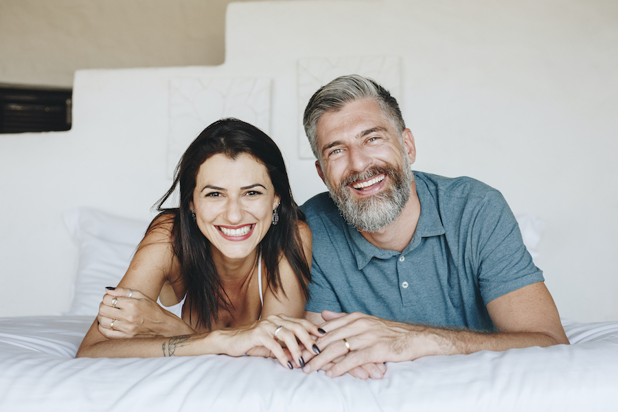 Middle-aged couple smile together on the bed with healthy, beautiful teeth