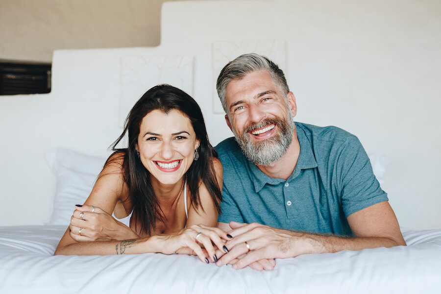 Middle-aged couple smile together on the bed with healthy, beautiful teeth