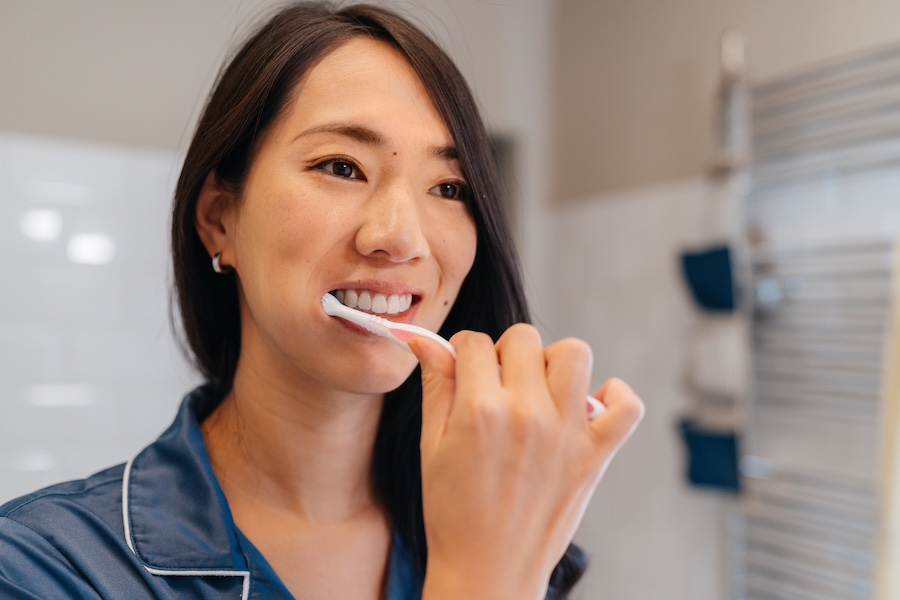Asian woman brushing her teeth and following tips for a healthy smile